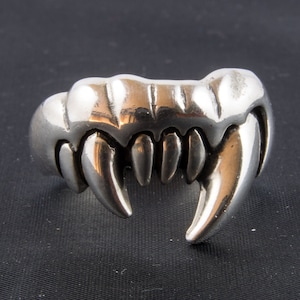 May include: A silver ring shaped like a set of sharp teeth. The ring is designed to look like a set of fangs.