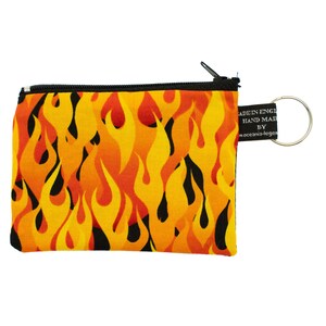 Puede incluir: Una pequeña bolsa negra con cremallera con un patrón de llamas en tonos naranja y amarillo. La bolsa tiene un llavero plateado unido a la cremallera.