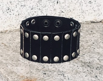 May include: A black leather bracelet with silver studs. The bracelet is wide and has a simple design.