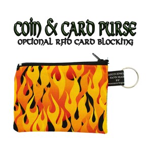 Può includere: Un piccolo portamonete e portacarte rettangolare con chiusura a zip. Presenta un vivace motivo a fiamme in giallo, arancione e nero. Il testo "COIN & CARD PURSE OPTIONAL RFID CARD BLOCKING" è sopra. Un piccolo tag e un portachiavi sono attaccati.