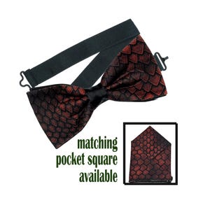 May include: A pre-tied bow tie featuring a dark red and black dragon scale pattern with a black adjustable elastic neck strap and metal hardware. The image includes a small inset showing a matching pocket square and the text matching pocket square available.