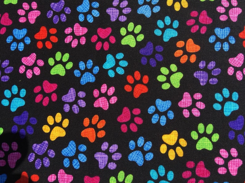 May include: A black fabric with a repeating pattern of colorful paw prints. The paw prints are in various colors, including red, orange, yellow, green, blue, purple, and pink.