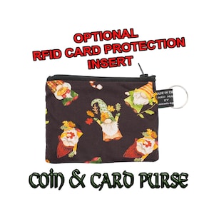 Könnte beinhalten: Eine kleine schwarze Reißverschluss-Münz- und Kartenbörse mit einem Gnom-Muster. Die Börse hat einen Metallring, der am Reißverschluss befestigt ist. Der Text "MADE IN EN" und "AND MA DY" ist auf einem Etikett gedruckt, das am Ring befestigt ist. Der Text "OPTIONAL RFID CARD PROTECTION INSERT" ist über der Börse gedruckt. Der Text "COIN & CARD PURSE" ist unter der Börse gedruckt.