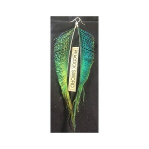 Puede incluir: Un par de aretes largos de plumas de pavo real verde y azul con alambre de plata. Los aretes están etiquetados como "PEACOCK SWORD".