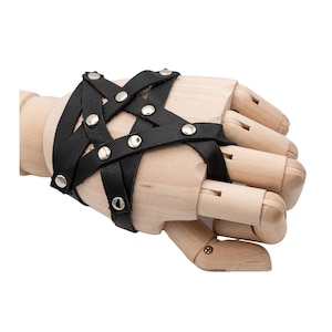 Könnte beinhalten: Schwarzes Leder-Handgeschirr mit silberfarbenen Nieten. Das Geschirr hat ein Kreuzmuster mit mehreren Riemen und ist mit Nieten befestigt. Das Accessoire wird auf einer hölzernen Handpuppe präsentiert.