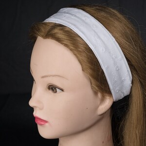 May include: White headband with a delicate embroidered pattern. The headband is made of soft fabric and is perfect for keeping hair out of your face.