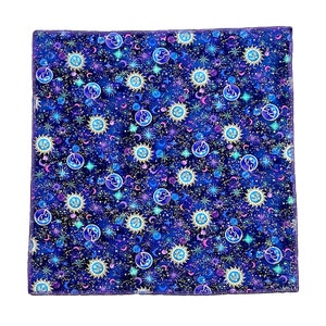 Può includere: Un quadrato di tessuto blu con un motivo ripetuto di stelle dorate, lune e soli. Lo sfondo è blu scuro con una sfumatura viola sottile.