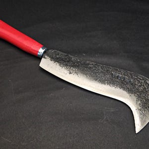 May include: A curved, silver-coloured blade with a red plastic handle. The blade has a textured surface and a slight curve at the tip. The handle is attached to the blade with a silver metal ring.