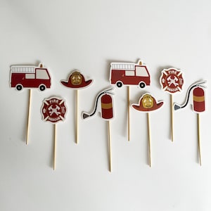 May include: Set of eight red and yellow fire truck themed cupcake toppers. The toppers feature a fire truck, a fire hydrant, a fire hat, and a fire rescue sign.