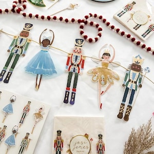 May include: A Nutcracker and Ballerina themed party garland with red and white pom poms. The garland features a string of nutcracker and ballerina figures with gold, red, blue, and green accents. The garland is perfect for a holiday party or celebration.