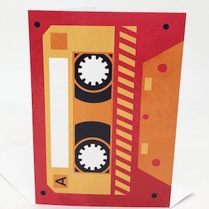 May include: A red and yellow cassette tape card with a black and white cassette tape design. The cassette tape has a label that says "A".