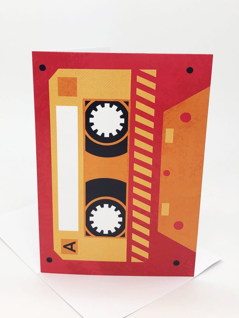 May include: A red and yellow cassette tape card with a black and white cassette tape design. The cassette tape has a label that says "A".