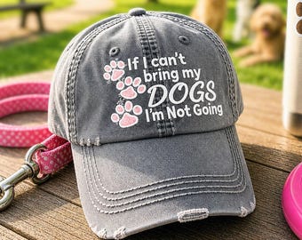 May include: A distressed gray baseball cap with the text "If I can't bring my DOGS I'm Not Going" and pink paw prints. A pink and white polka dot dog leash, a water bottle with a paw print, and a pink frisbee are also visible.