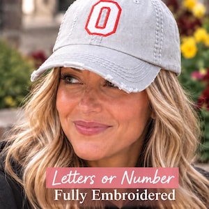May include: A light gray baseball cap with a distressed, worn-in finish. The front panel features a large, bold, fully embroidered letter O in bright red with a white outline. The cap has a curved brim with frayed edges and a structured crown.