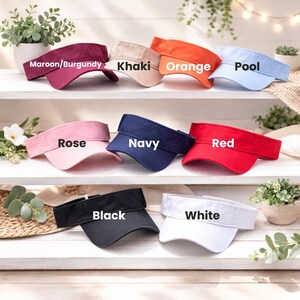 A collection of colorful visor hats is displayed on a shelf, each with a different color and labeled with the corresponding color name.