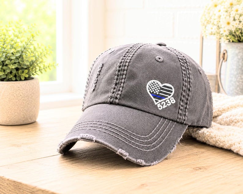 May include: Distressed gray baseball cap with a heart-shaped emblem featuring a blue line, black and white checkered pattern, and the number 5238. The cap has a curved brim and visible stitching details.