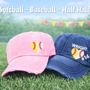 May include: Two baseball caps, one pink and one navy blue, rest on green grass. Each cap features a heart-shaped design combining a softball and baseball. The navy cap has the name "WRIGHT" and the number "14". The text "Softball - Baseball - Half Half" is at the top.