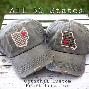 May include: Two distressed gray baseball caps with state outlines and red heart accents. One features Ohio, the other Missouri, with the text "All 50 States" and "Optional Custom Heart Location".