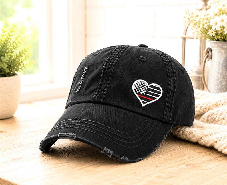 May include: Black distressed baseball cap with a heart-shaped patch. The patch features a design with a white and black checkered pattern, a red stripe, and white stripes. The cap has a curved brim and a worn, vintage look.