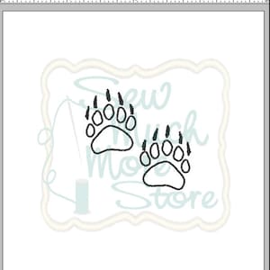 Może przedstawiać: Dwa czarne ślady łap niedźwiedzia na białym tle. Ślady łap są obwiedzione czarną linią i mają po pięć palców.