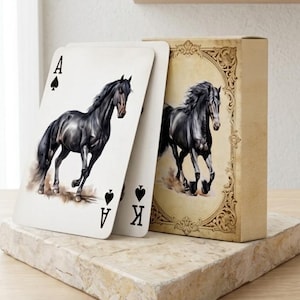 Peut inclure: Un jeu de cartes à jouer illustré d'un cheval noir sur l'as de pique et sur l'étui. La boîte présente un cadre ornementé de style vintage sur fond beige. Les cartes sont blanches avec des symboles de pique noirs et les lettres A et K.