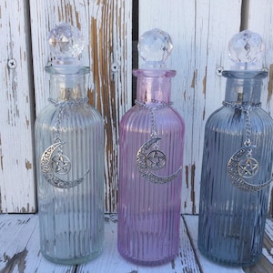 Peut inclure: Trois bouteilles en verre avec des motifs côtelés et des bouchons en cristal. Chaque bouteille a un charme argenté suspendu, représentant une lune croissante et une étoile à cinq branches.