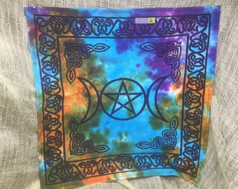 May include: A tie-dye tapestry with a blue background and a black pentacle with three moons. The tapestry has a black border with a Celtic knot design.