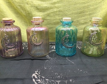 May include: Four glass bottles with cork stoppers and a crescent moon charm hanging from each. The bottles are iridescent and come in shades of purple, pink, blue, and green.