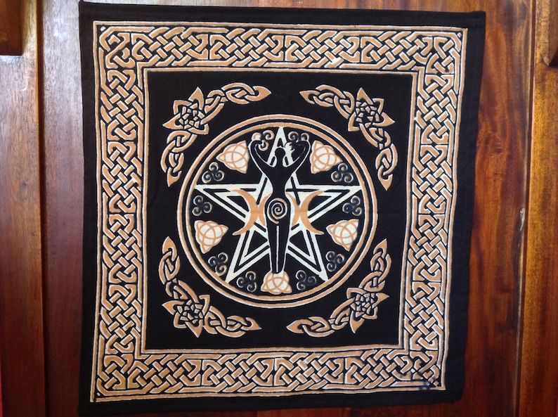 K&ouml;nnte beinhalten: Ein schwarzer Stoffteppich mit einem goldenen keltischen Knotenrand. In der Mitte befindet sich ein wei&szlig;es Pentagramm mit einer weiblichen Figur darin. Die Figur ist von drei Mondsicheln und drei Triskelen umgeben.