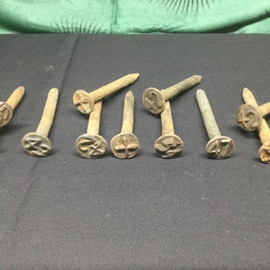 May include: Ten rusty metal nails with a cross-shaped head and a number stamped on each head. The numbers range from 41 to 49.