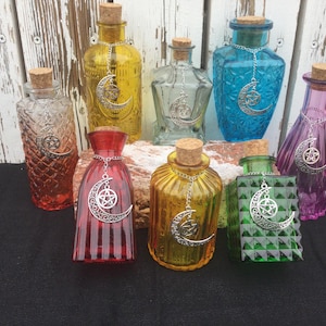 May include: A selection of coloured glass bottles with cork stoppers. Each bottle is decorated with a silver charm featuring a crescent moon and a five-pointed star. The bottles vary in shape and colour, including red, yellow, and green.