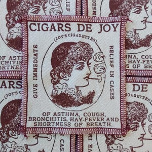 Könnte beinhalten: Ein rechteckiger Stoffaufnäher mit cremefarbenem Hintergrund und dunkelrotem Text sowie Illustration. In der Mitte ist das Profil einer rauchenden Person abgebildet, umgeben vom Text CIGARS DE JOY, JOY'S CIGARETTES und medizinischen Angaben.