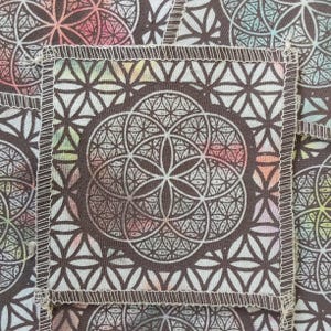May include: A square fabric patch featuring a dark brown geometric flower of life pattern printed over a multicolored background. The edges of the patch are finished with a white overlock stitch, creating a distinct border around the design.