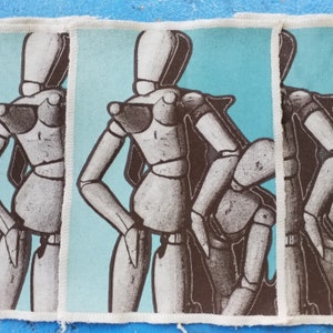 May include: Three fabric patches with a blue background and a white outline. Each patch features a black and white illustration of a stylised female figure with a brown bodice.