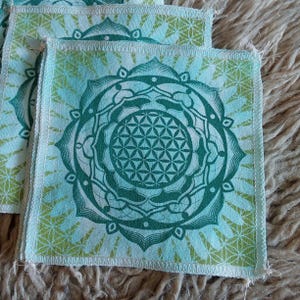 Puede incluir: Parches cuadrados de tela con un diseño floral verde y turquesa. Los parches presentan un patrón central tipo mandala con un diseño geométrico de flor de la vida. Los bordes están acabados con una costura blanca.