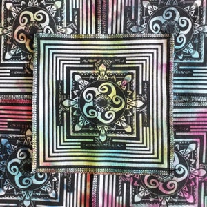 May include: Square textile with a black and white geometric design. The centre features a square with concentric lines and a circular, swirling pattern. The corners have similar circular designs. The background has vertical stripes and watercolour-like splashes of colour.