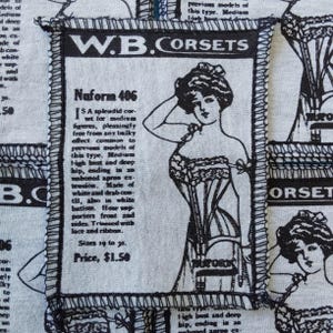 May include: A fabric panel featuring a vintage advertisement for "W.B. Corsets." The black and white illustration depicts a woman in a corset, with text describing the product's features and sizing. The panel has a stitched border.