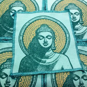 May include: A set of four teal blue fabric squares with a gold mandala design and a printed image of a meditating Buddha in the center of each square.