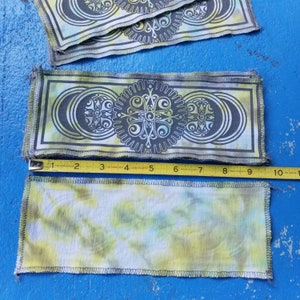 Op de afbeelding: Twee stoffen patches met een tie-dye patroon en een geometrisch ontwerp. Het geometrische ontwerp is in zwart en wit en heeft een cirkel met een kruis erin. De tie-dye patch is geel, groen en wit.