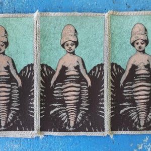 May include: Three fabric patches featuring a repeated image of a mermaid-like figure with a mushroom-shaped head. The figure is wearing a shell-like garment and has a striped tail. The background is a light blue-green colour.