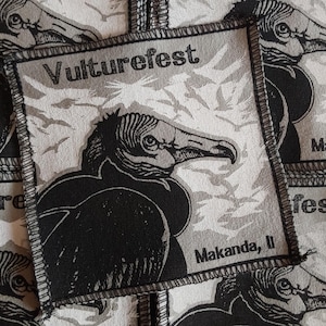 May include: Square patch with a black and white vulture illustration. The patch has the text "Vulturefest" at the top and "Makanda, Il" at the bottom. The background has a pattern of flying birds.
