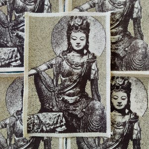 Pode incluir: Uma coleção de patches de tecido bege e castanho com uma figura de Buda sentado com um halo. Os patches têm uma borda creme e uma ilustração detalhada do Buda em pose meditativa.
