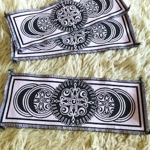 May include: Three black and white fabric patches with a repeating pattern of circles and swirls on a light purple background. The patches have a decorative stitched edge.