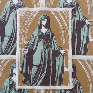 May include: A rectangular fabric patch featuring a screen-printed illustration of a figure in a draped robe and head covering, standing within an arched architectural frame. The design uses a color palette of muted sage green and dark brown.
