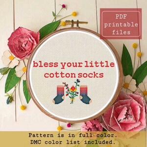 Può includere: Uno schema di ricamo a punto croce che presenta un paio di calzini con un mazzo di fiori tra loro. Il testo "bless your little cotton socks" è sopra i calzini. Lo schema è a colori e include un elenco di colori DMC.