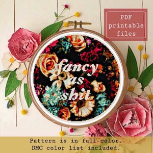 Può includere: Uno schema di punto croce con un design floreale e il testo "Fancy as shit" in bianco su sfondo nero. Lo schema è in un cerchio e circondato da fiori rosa e gialli.