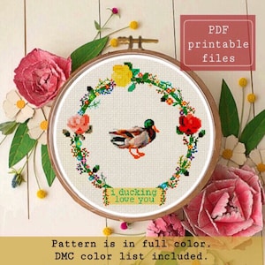 Può includere: Schema di punto croce con un'anatra con una ghirlanda di fiori intorno. Lo schema include il testo "I ducking love you".
