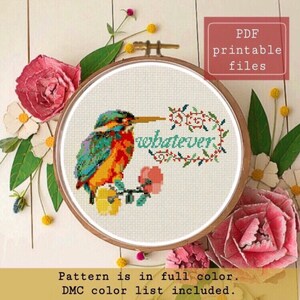 Può includere: Schema di punto croce con un martin pescatore colorato appollaiato su un ramo con fiori e la parola "whatever" in una cornice floreale. File PDF stampabile.