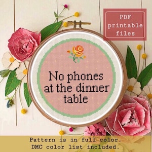 Può includere: Un motivo a punto croce rosa e verde con il testo "No phones at the dinner table" e un piccolo fiore arancione. Il motivo è in un telaio da ricamo in legno. Il testo "PDF printable files" è in un riquadro rosso nell'angolo in alto a destra dell'immagine. Il testo "Pattern is in full color. DMC color list included. www.etsy.com/shop/SamwiseSimpleStitch" è nella parte inferiore dell'immagine.