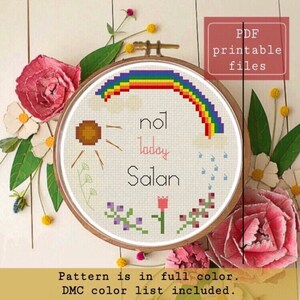 Può includere: Schema di punto croce con un arcobaleno, un sole, fiori e il testo "not today Satan". Lo schema è a colori e include un elenco di colori DMC.